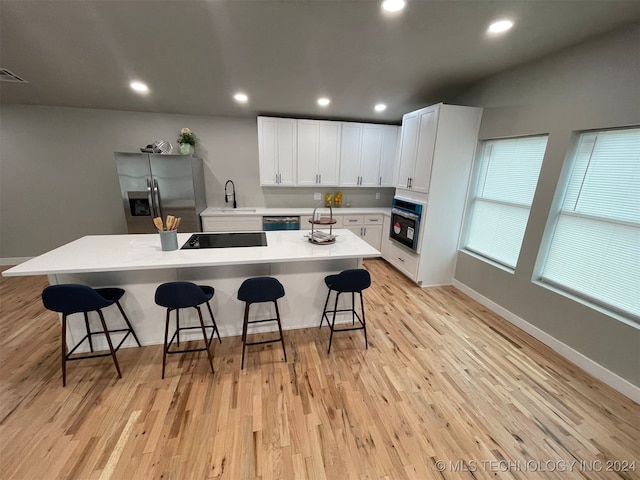 kitchen featuring black appliances, a center island with sink, light wood-type flooring, white cabinetry, and a breakfast bar area