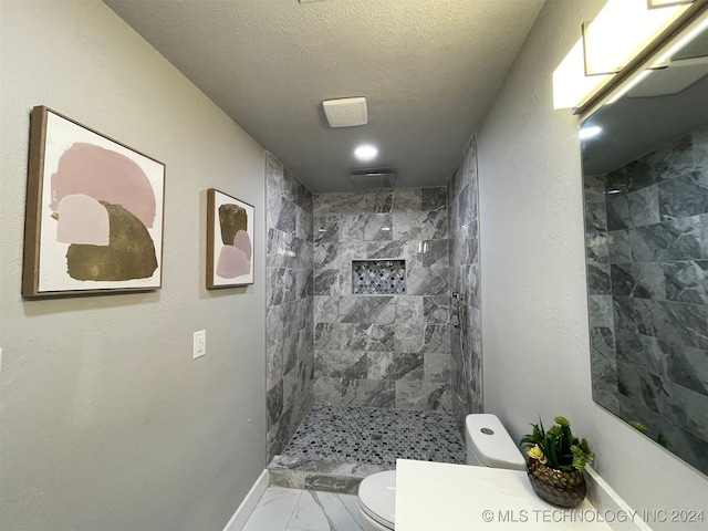 bathroom featuring a tile shower, a textured ceiling, and toilet