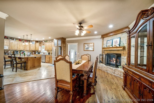 dining area featuring a stone fireplace, light hardwood / wood-style floors, and ceiling fan