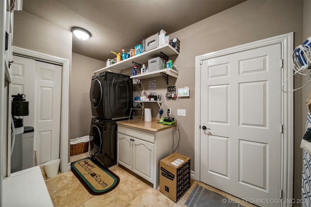 clothes washing area featuring stacked washer / drying machine and cabinets