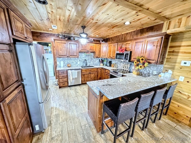 kitchen featuring kitchen peninsula, stainless steel appliances, sink, light hardwood / wood-style flooring, and wood walls