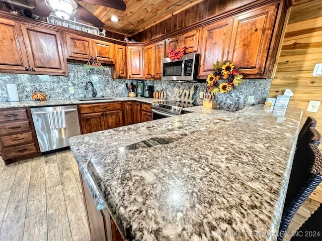 kitchen featuring light wood-type flooring, stainless steel appliances, light stone counters, and sink