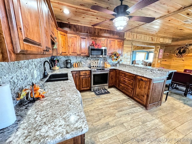 kitchen featuring light stone countertops, sink, stainless steel appliances, kitchen peninsula, and wooden walls