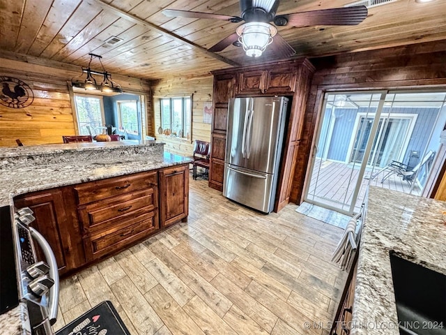 kitchen with wooden ceiling, light stone counters, stainless steel fridge, wooden walls, and light wood-type flooring