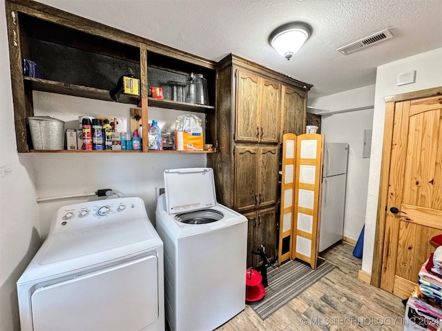 clothes washing area with separate washer and dryer, cabinets, a textured ceiling, and light wood-type flooring