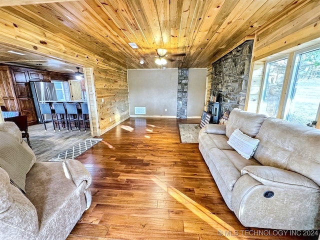 living room with wood-type flooring, a wood stove, wooden ceiling, and wood walls