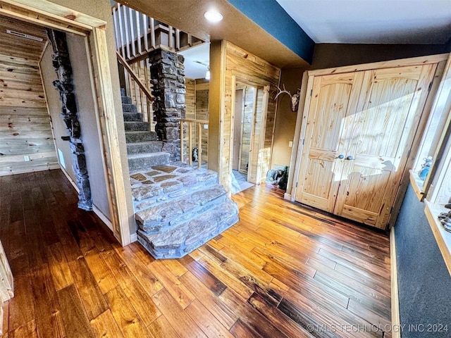 foyer entrance featuring hardwood / wood-style flooring, vaulted ceiling, and wood walls