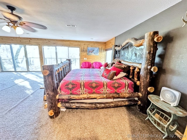 bedroom featuring carpet flooring, ceiling fan, wood walls, and a textured ceiling