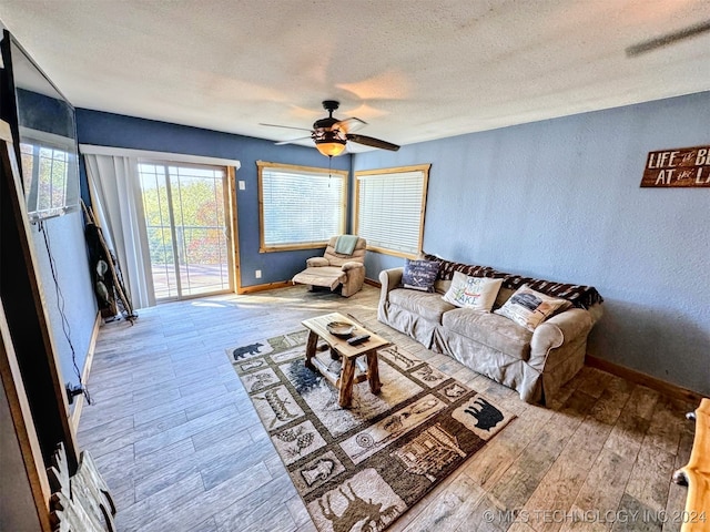 living room featuring ceiling fan, light wood-type flooring, and a textured ceiling