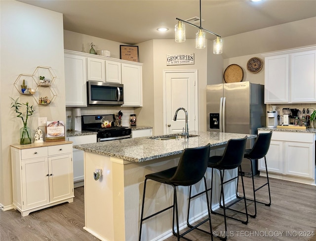 kitchen featuring hardwood / wood-style floors, a kitchen island with sink, white cabinets, sink, and stainless steel appliances