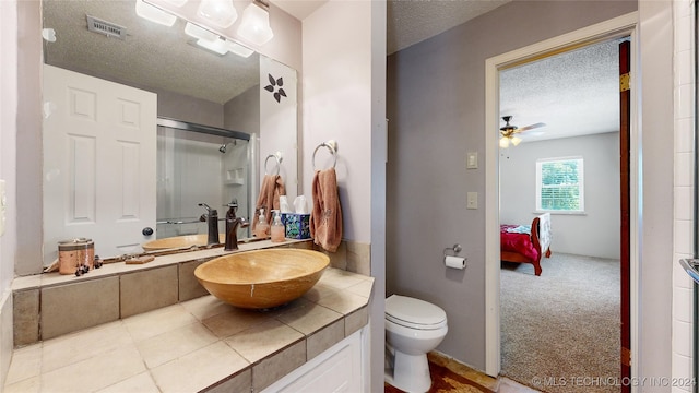 bathroom with tile patterned flooring, ceiling fan, toilet, a textured ceiling, and a shower with shower door