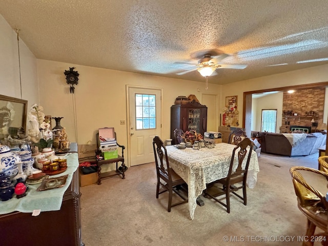 dining room with a fireplace, a textured ceiling, light colored carpet, and ceiling fan