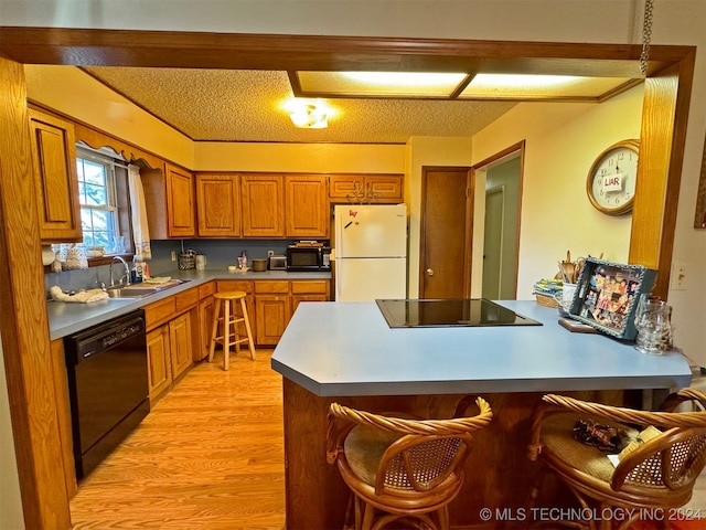 kitchen featuring a kitchen bar, a textured ceiling, sink, black appliances, and light hardwood / wood-style flooring