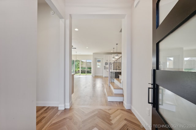 hallway with light parquet floors and an inviting chandelier