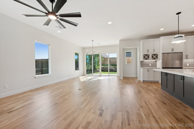 unfurnished living room with ceiling fan with notable chandelier and light hardwood / wood-style floors