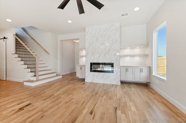 unfurnished living room with light wood-type flooring, a barn door, ceiling fan, and a premium fireplace