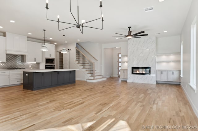 kitchen with a large island, wall oven, a premium fireplace, white cabinets, and pendant lighting