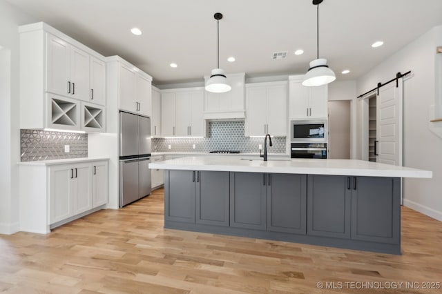 kitchen featuring sink, white cabinetry, black appliances, a barn door, and a kitchen island with sink