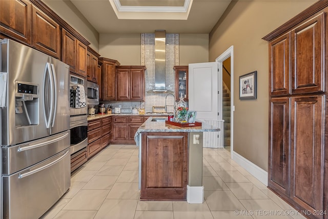 kitchen featuring a raised ceiling, wall chimney exhaust hood, light tile patterned floors, appliances with stainless steel finishes, and a kitchen island