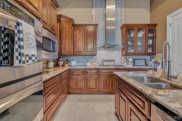 kitchen featuring appliances with stainless steel finishes, backsplash, light stone counters, sink, and wall chimney range hood