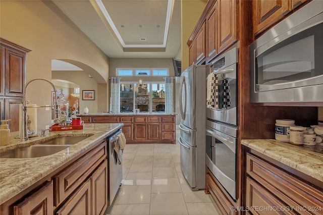 kitchen featuring appliances with stainless steel finishes, light stone counters, a raised ceiling, sink, and light tile patterned flooring