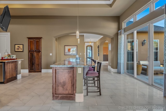 kitchen with a center island with sink, light stone countertops, a breakfast bar area, and ornamental molding