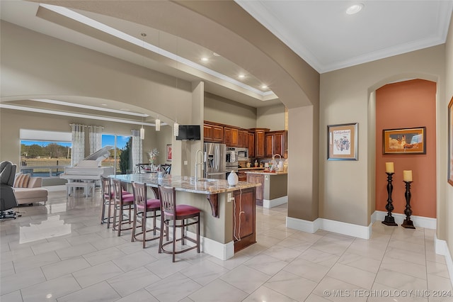 kitchen featuring a breakfast bar, a center island, crown molding, light stone countertops, and light tile patterned flooring