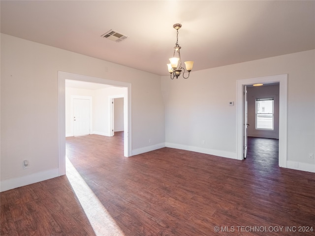 empty room with dark hardwood / wood-style flooring and a notable chandelier