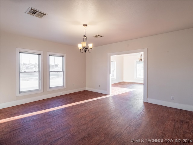 spare room with dark wood-type flooring and an inviting chandelier