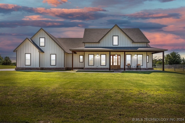 back house at dusk featuring a lawn and a porch