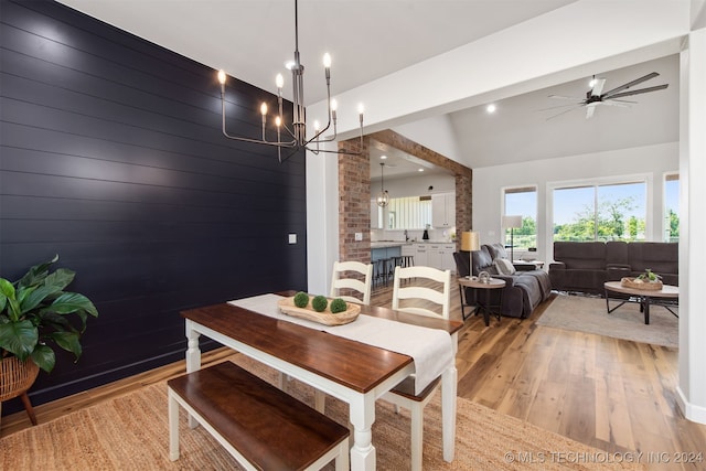 dining room with ceiling fan with notable chandelier, light hardwood / wood-style floors, lofted ceiling, and wood walls