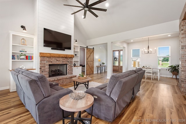 living room featuring high vaulted ceiling, ceiling fan with notable chandelier, a barn door, a fireplace, and light hardwood / wood-style floors