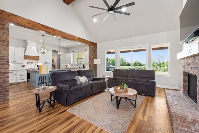 living room with ceiling fan, hardwood / wood-style floors, high vaulted ceiling, and a brick fireplace