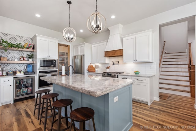 kitchen featuring backsplash, an island with sink, white cabinetry, stainless steel appliances, and beverage cooler