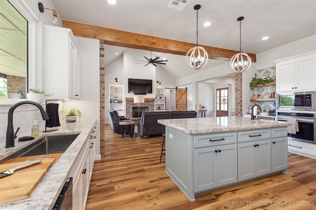 kitchen with a center island with sink, white cabinets, lofted ceiling with beams, and appliances with stainless steel finishes