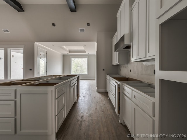 kitchen featuring white cabinetry, a raised ceiling, wood-type flooring, and beam ceiling