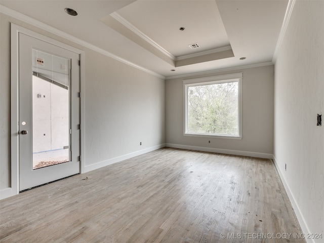 empty room with a raised ceiling, light hardwood / wood-style flooring, and ornamental molding