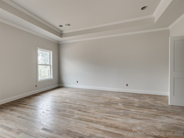 unfurnished room with light wood-type flooring, a raised ceiling, and crown molding