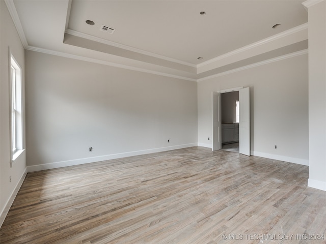 empty room featuring a tray ceiling, light hardwood / wood-style flooring, and ornamental molding