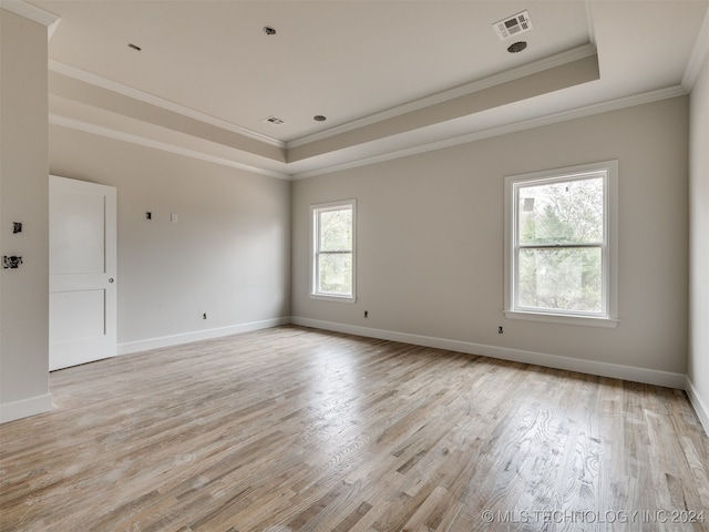 unfurnished room featuring a tray ceiling, crown molding, and light wood-type flooring