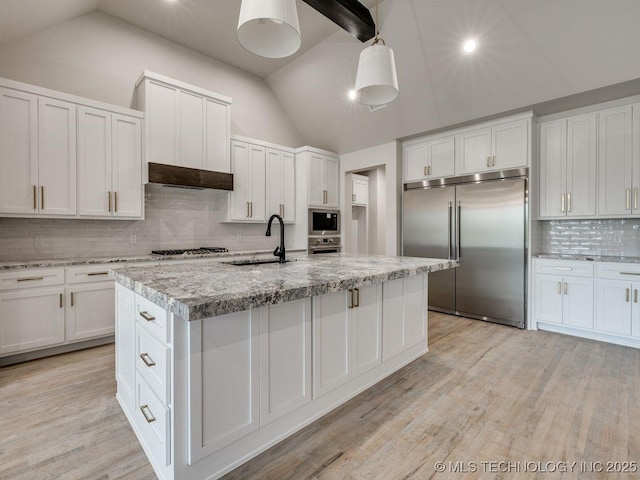 kitchen featuring built in appliances, sink, white cabinets, and a center island with sink