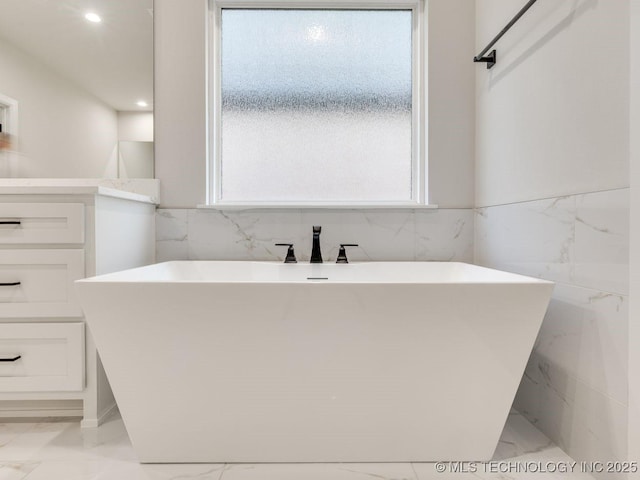 bathroom featuring tile walls, a bath, and vanity