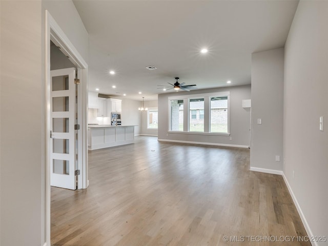 unfurnished living room featuring baseboards, light wood-style flooring, visible vents, and ceiling fan with notable chandelier