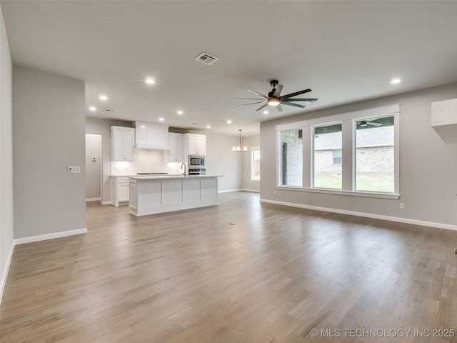 unfurnished living room featuring ceiling fan with notable chandelier, baseboards, visible vents, and recessed lighting