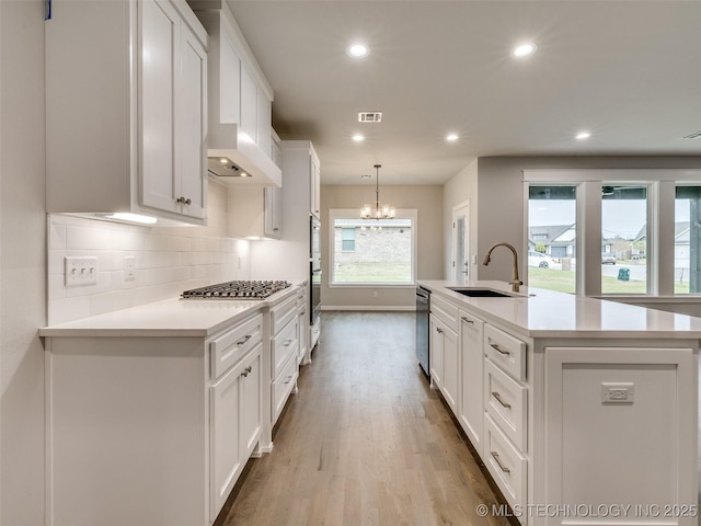 kitchen featuring stainless steel gas stovetop, light countertops, wood finished floors, a sink, and white cabinetry