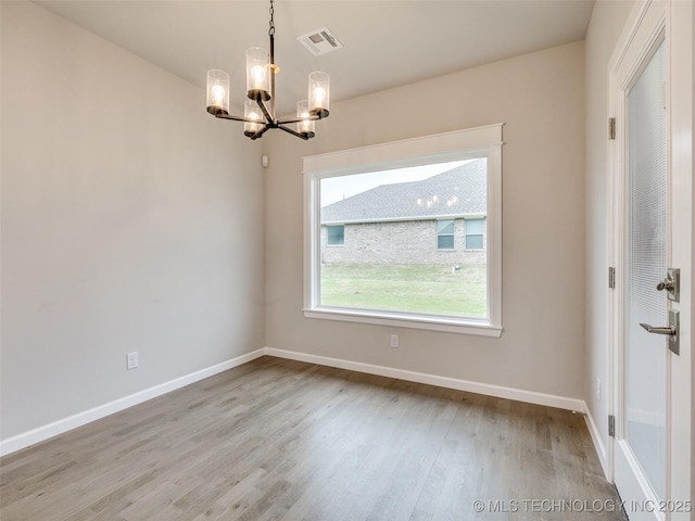 unfurnished room with baseboards, a notable chandelier, wood finished floors, and visible vents
