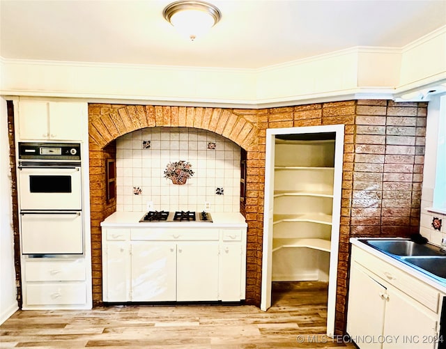 kitchen with stainless steel gas stovetop, backsplash, white cabinets, crown molding, and light wood-type flooring