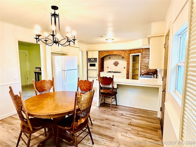 dining space with sink, light hardwood / wood-style floors, crown molding, and a notable chandelier