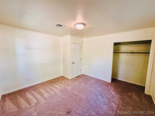 unfurnished bedroom featuring dark colored carpet, crown molding, and a closet