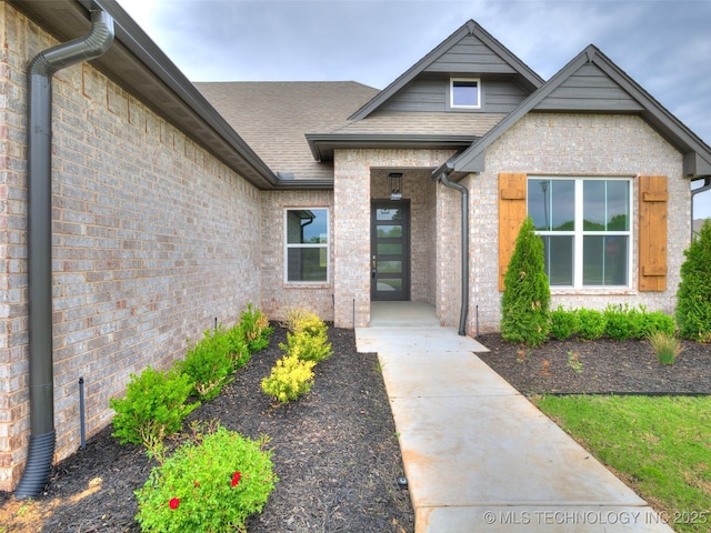 doorway to property featuring a shingled roof and brick siding